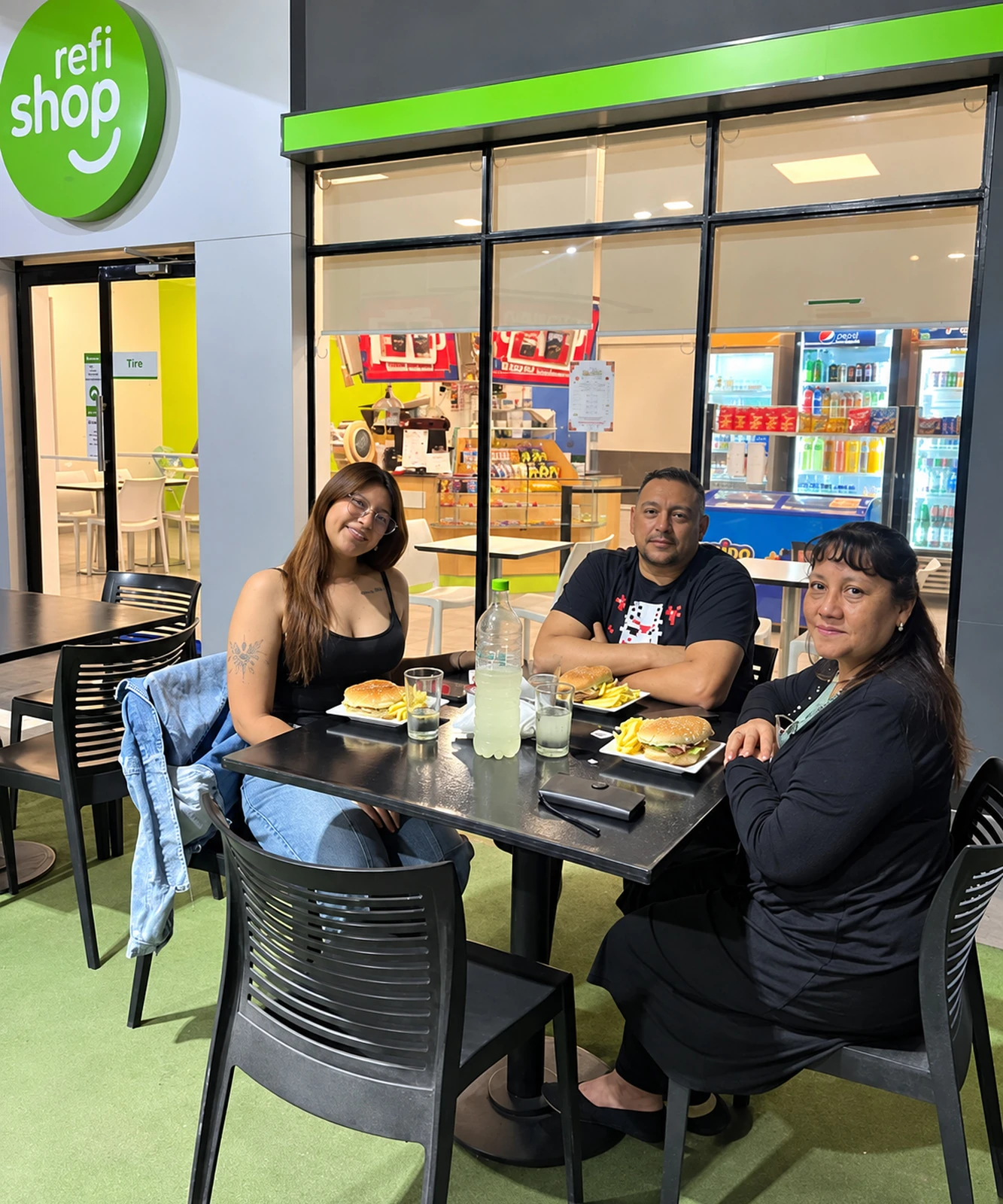 Clientes compartiendo una comida en las mesas exteriores de RefiShop Aguaray